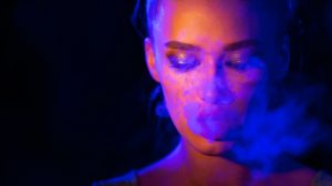 Mysterious girl smoking e-cigarette in neon blue and orange light
